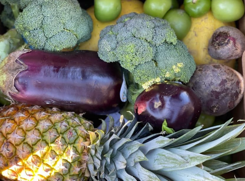 Fresh broccoli, eggplant, pineapple, beets and green tomatoes packed close together in a box
