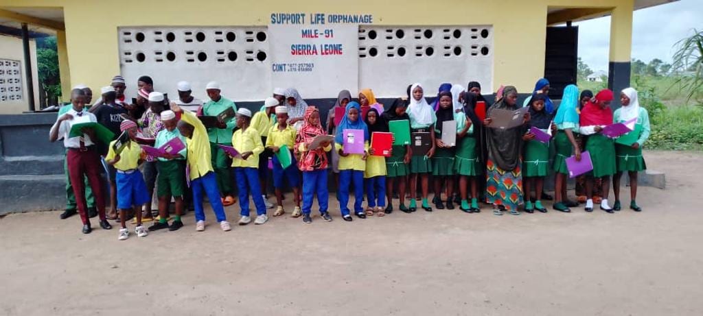 Children and staff of the Support Life Orphanage lined up together outside the building