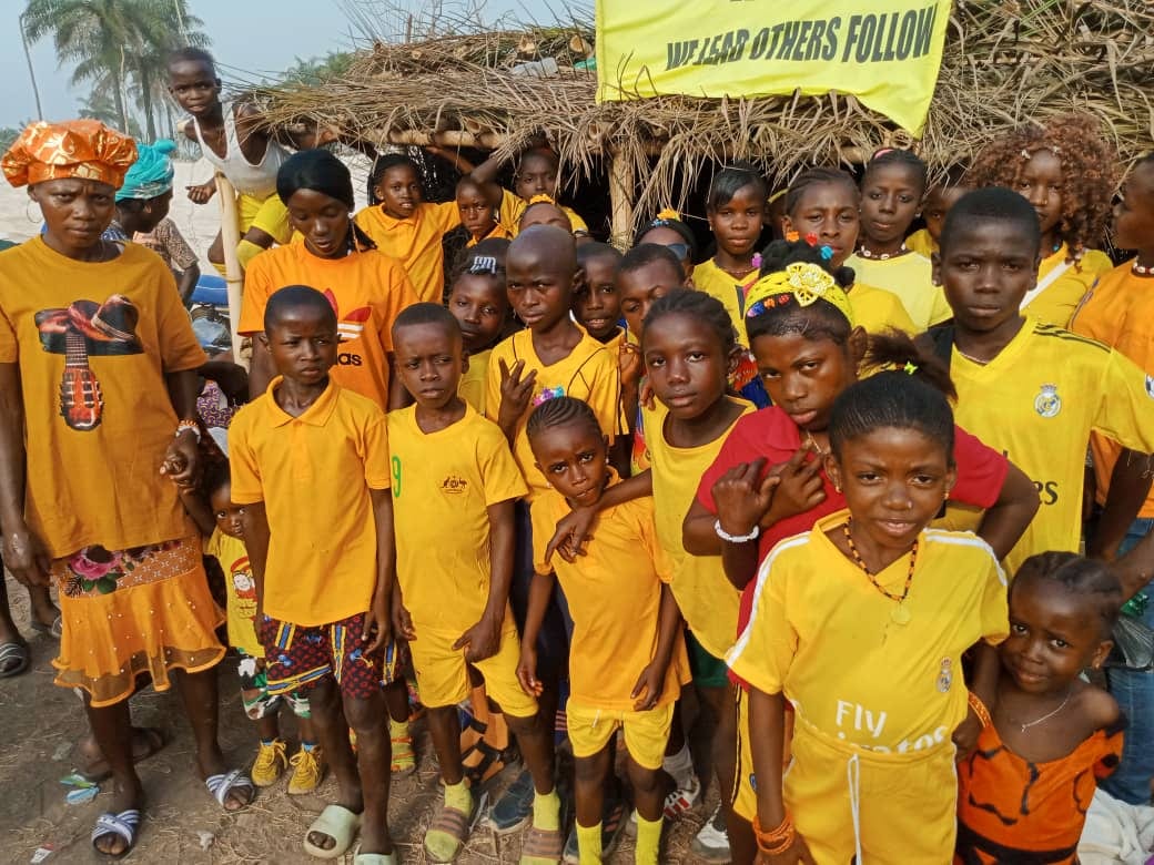 School children in yellow uniforms gathered under a banner outside their classroom