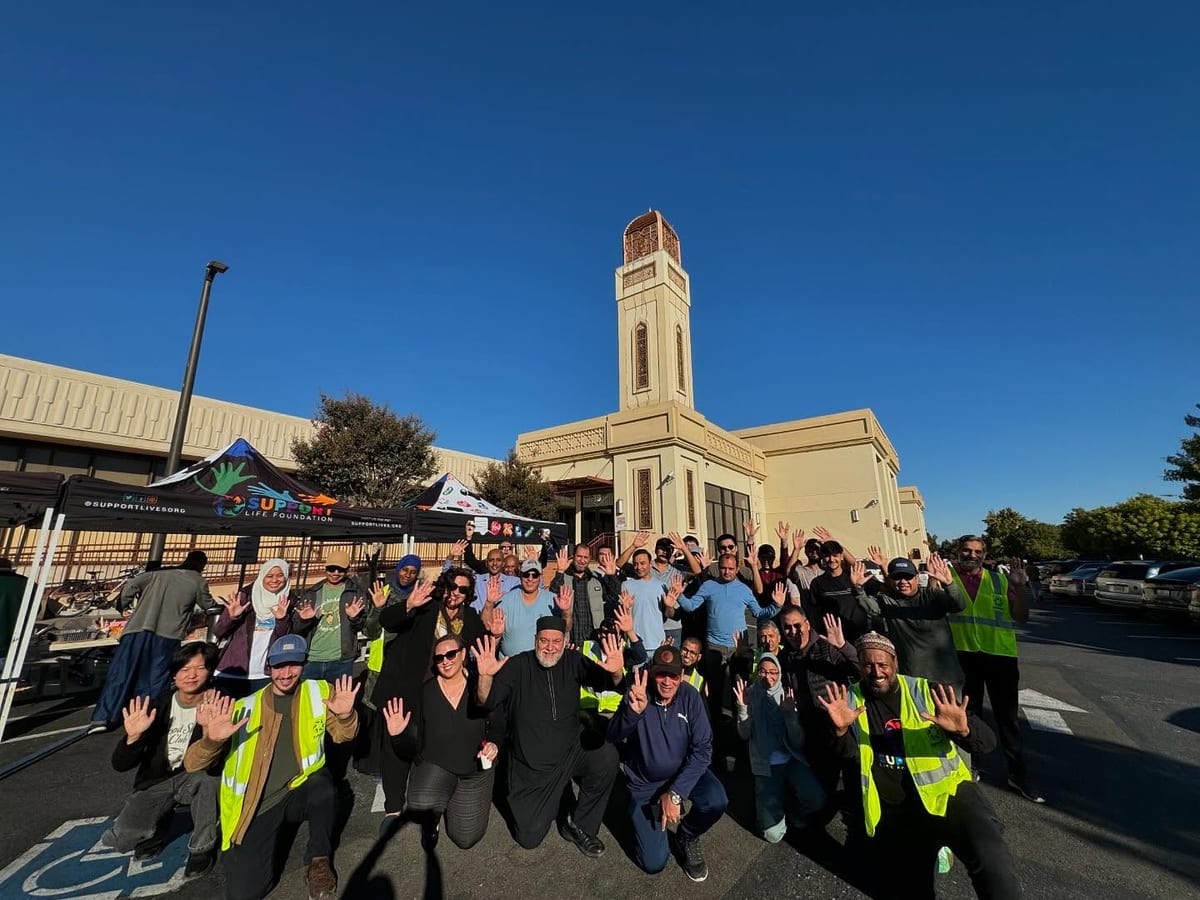 A large crowd of YANA volunteers gathered in a mosque car park with their hands raised, ready for a delivery morning