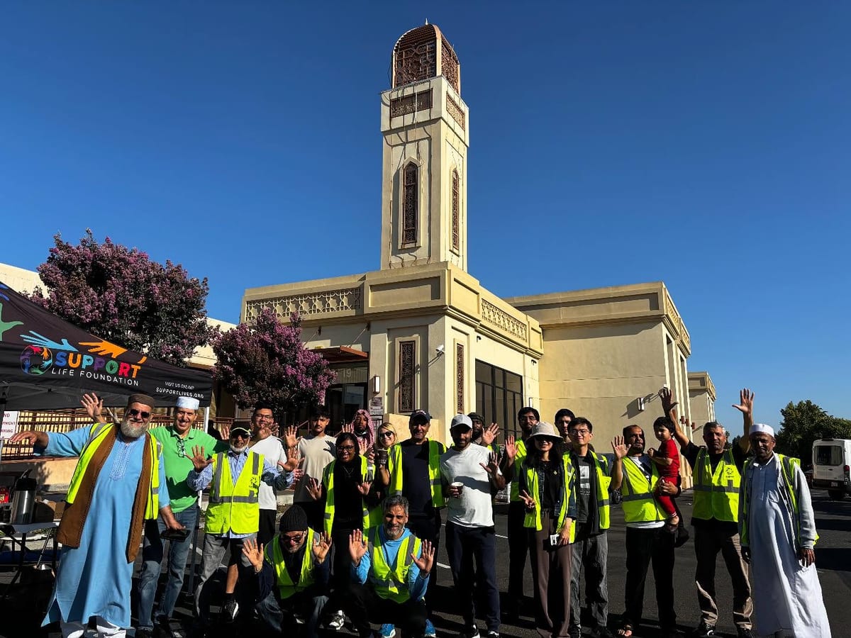A large crew of volunteers in high-visibility vests gathered outside a mosque on a bright morning, ready to load and drive a delivery run