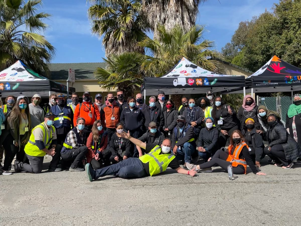 A large group of Support Life Foundation volunteers in black shirts and high-visibility vests photographed together at night after a delivery run