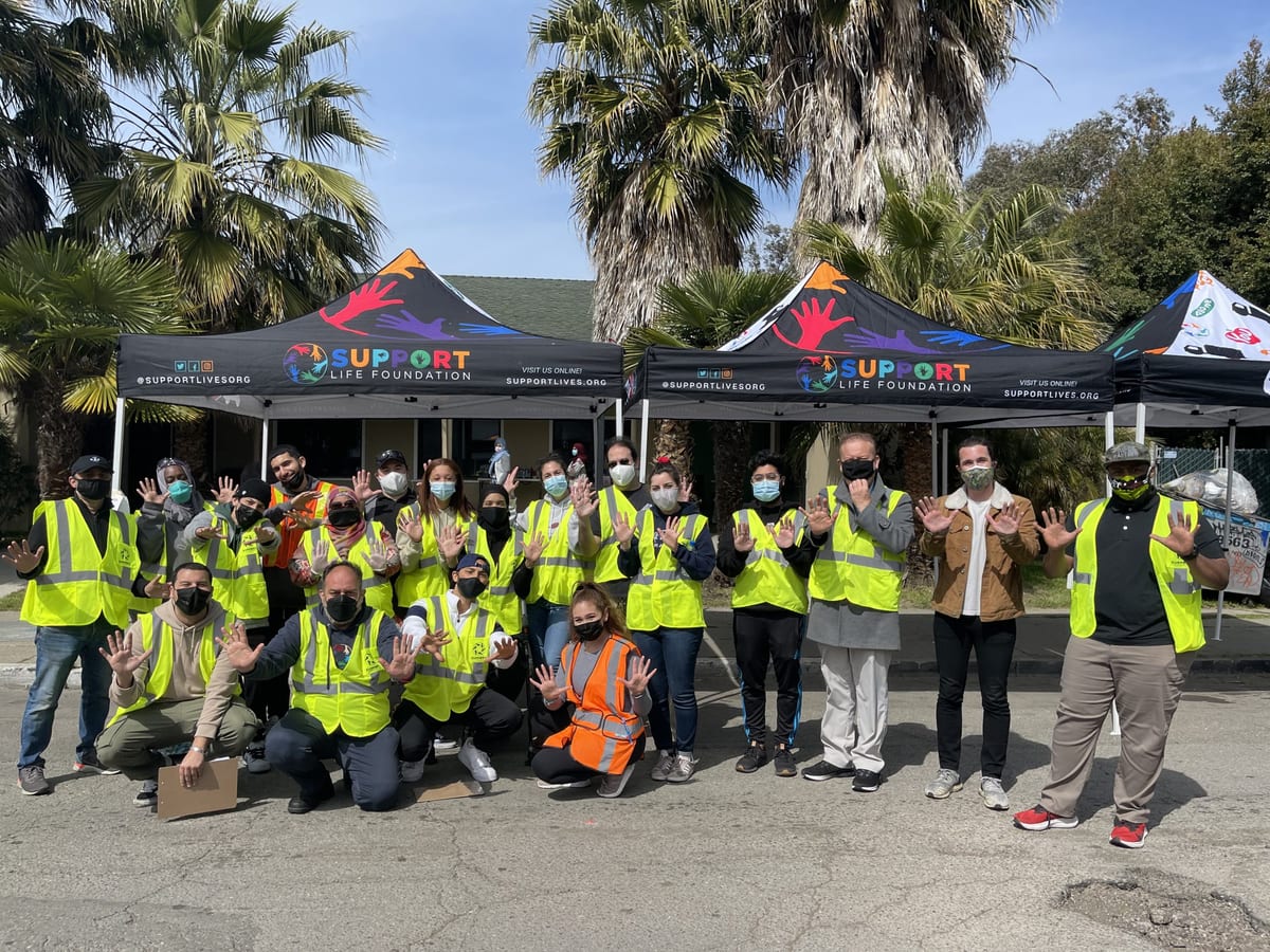 Support Life Foundation volunteers in yellow safety vests standing together outside under branded tents before a grocery delivery run